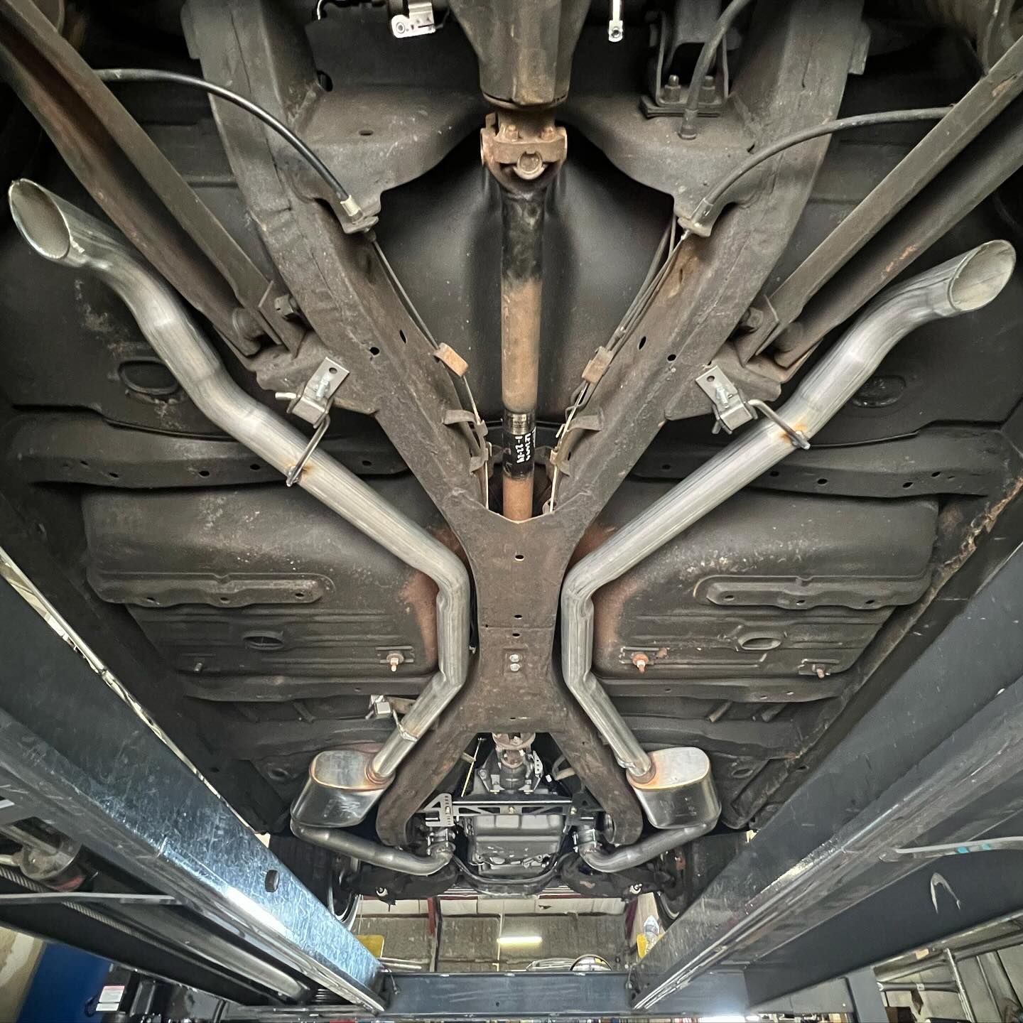 Undercarriage view of a vehicle on a lift, showing the exhaust system, frame, and drivetrain components.