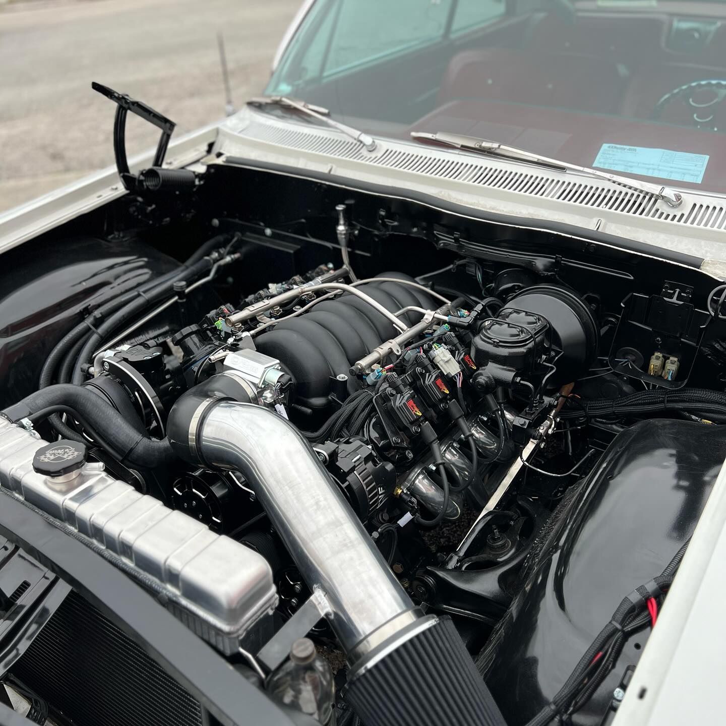 White classic car engine bay with black engine and silver intake.