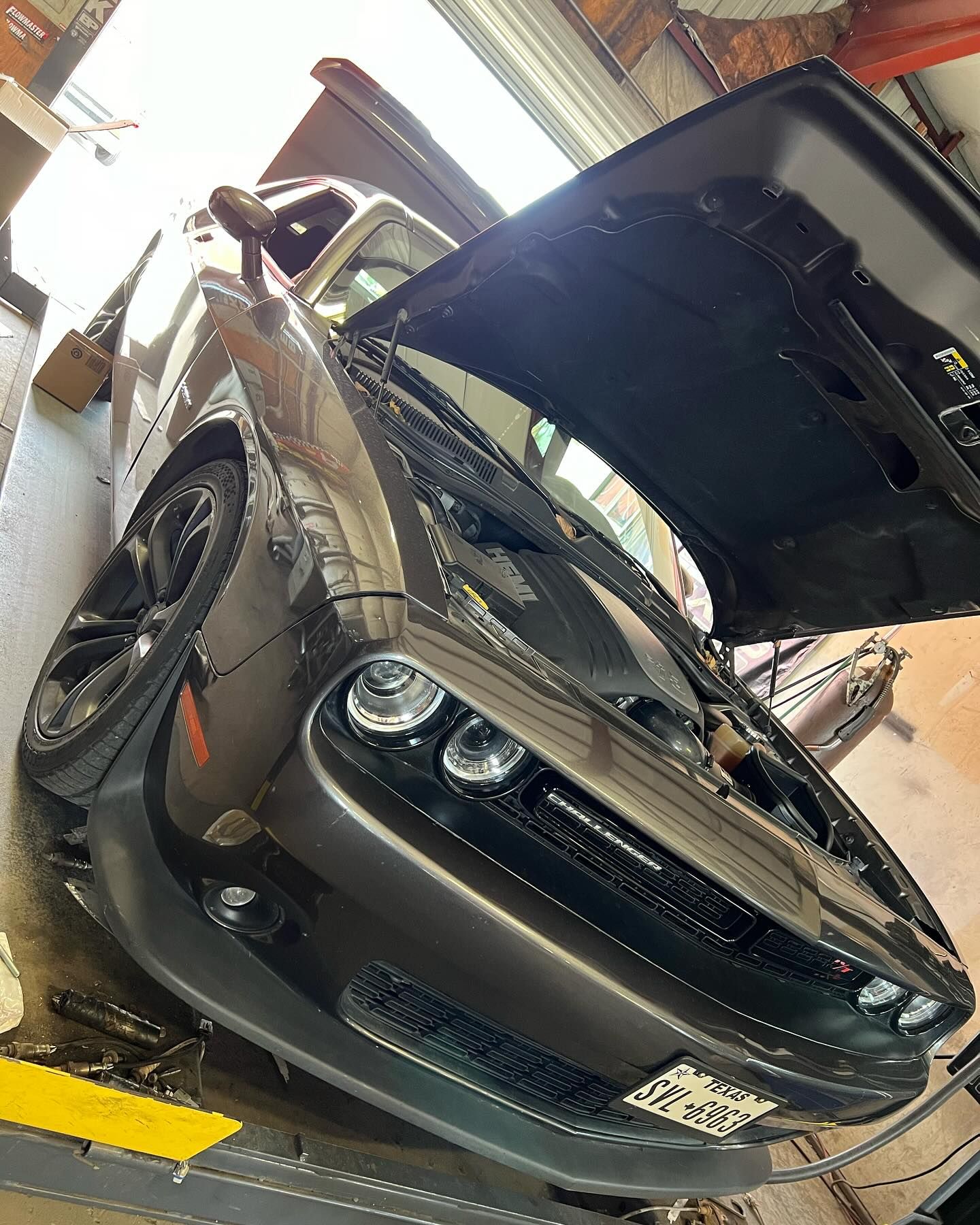 Gray Dodge Challenger with hood open inside a repair shop.