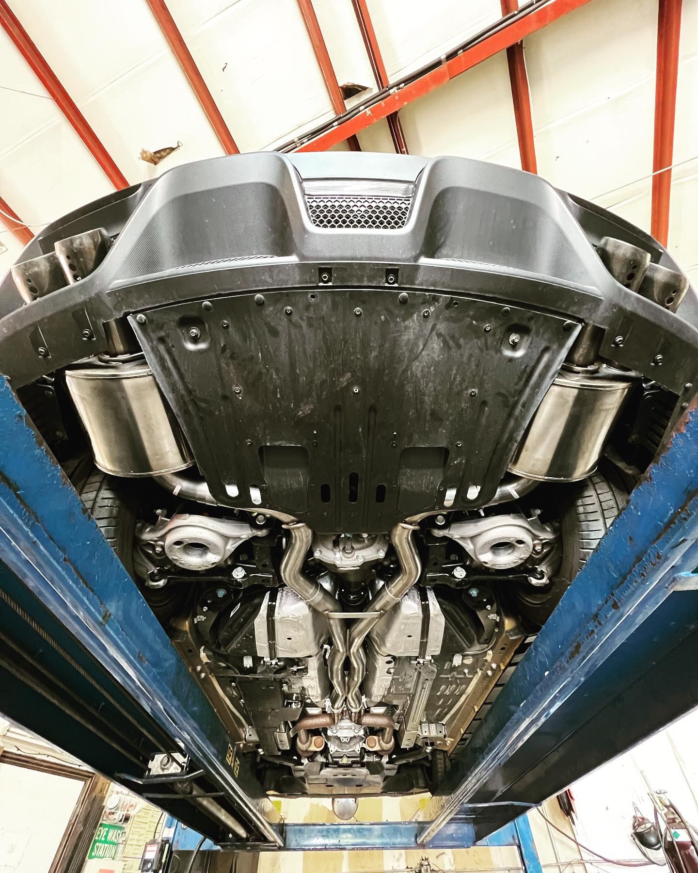 Underside of a car on a lift; visible exhaust system and undercarriage. Black, gray, and silver components.