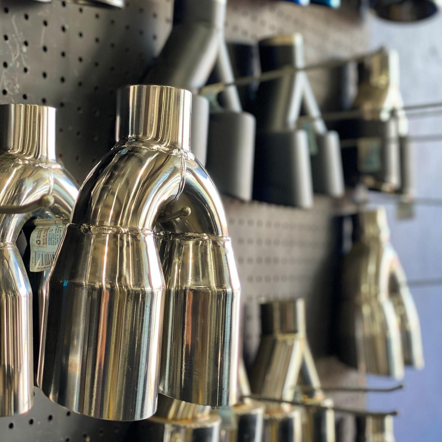 Shiny, chrome exhaust tips on display at a store, mounted on a pegboard.