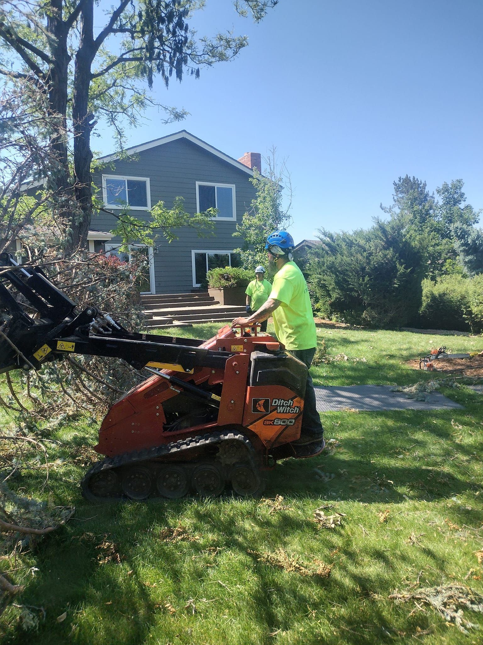 A person in a green shirt operating a mini trencher in a yard. A house is in the background.