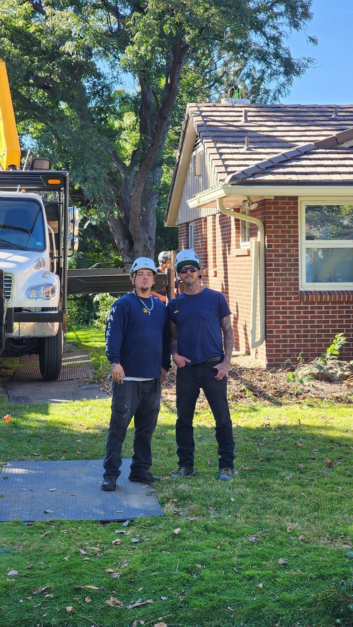 Two men in work clothes stand in front of a house, next to a truck.