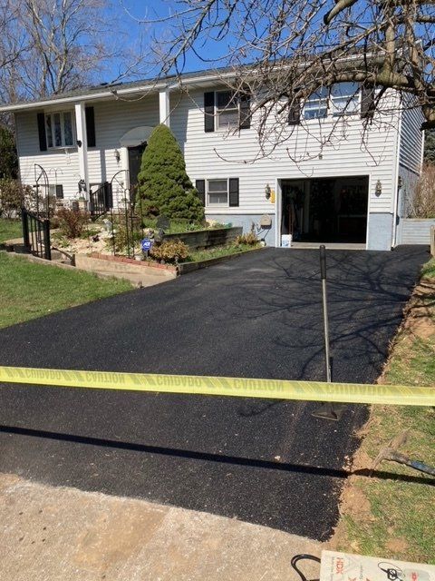 A white house with a black driveway is behind a yellow tape