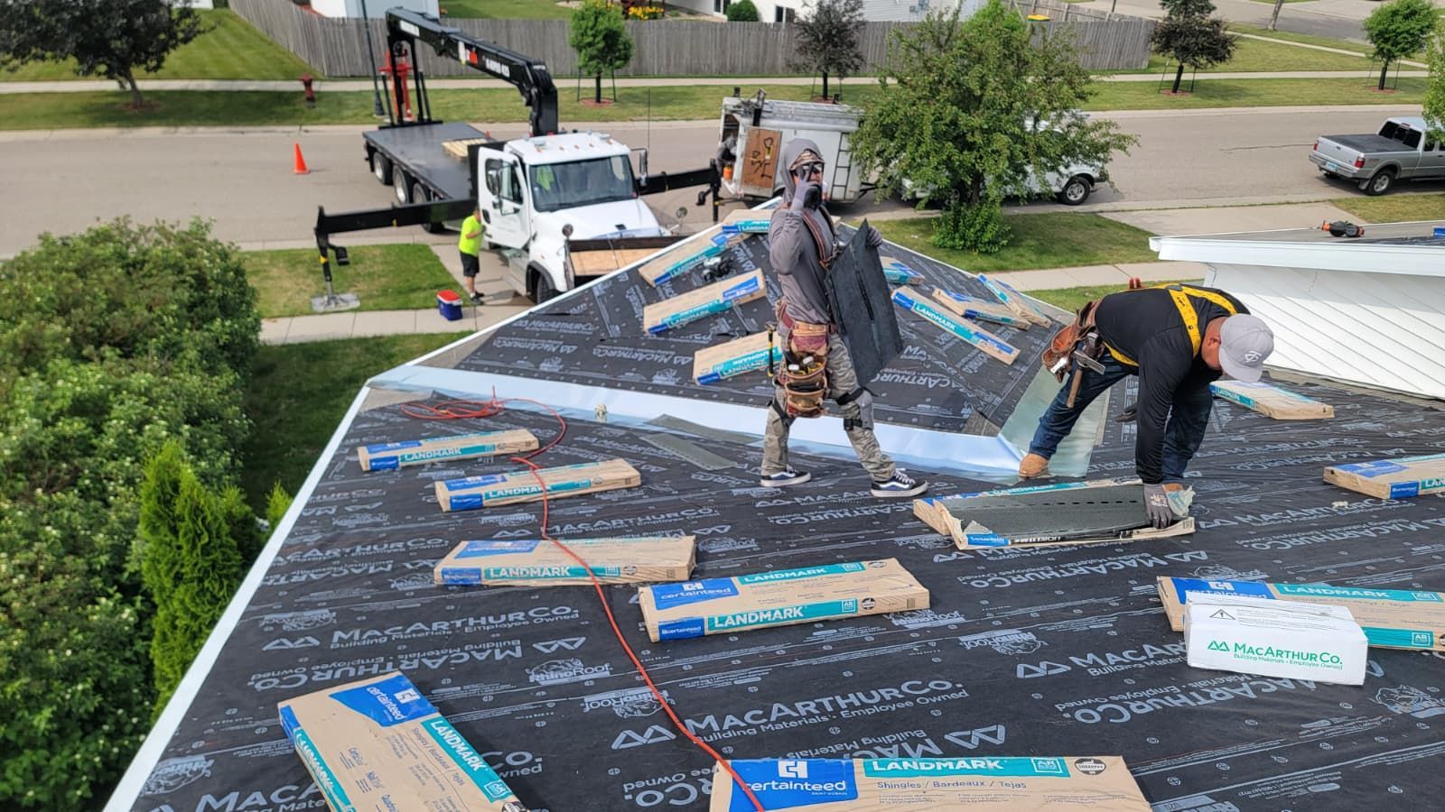 Workers installing roofing on a house, with shingles and tools spread across the roof.