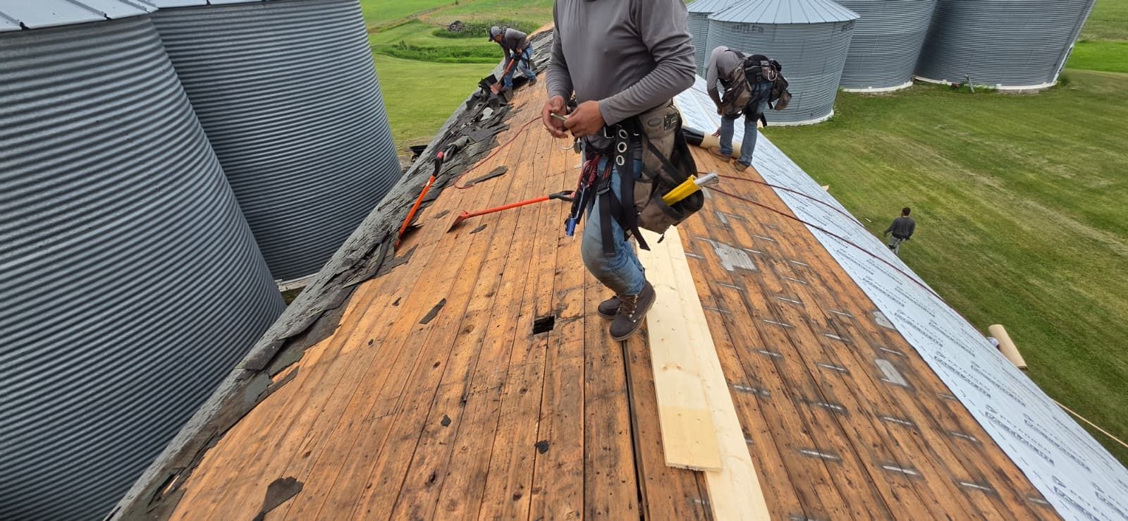 Workers repairing a wooden roof with tools and materials on a steep rooftop