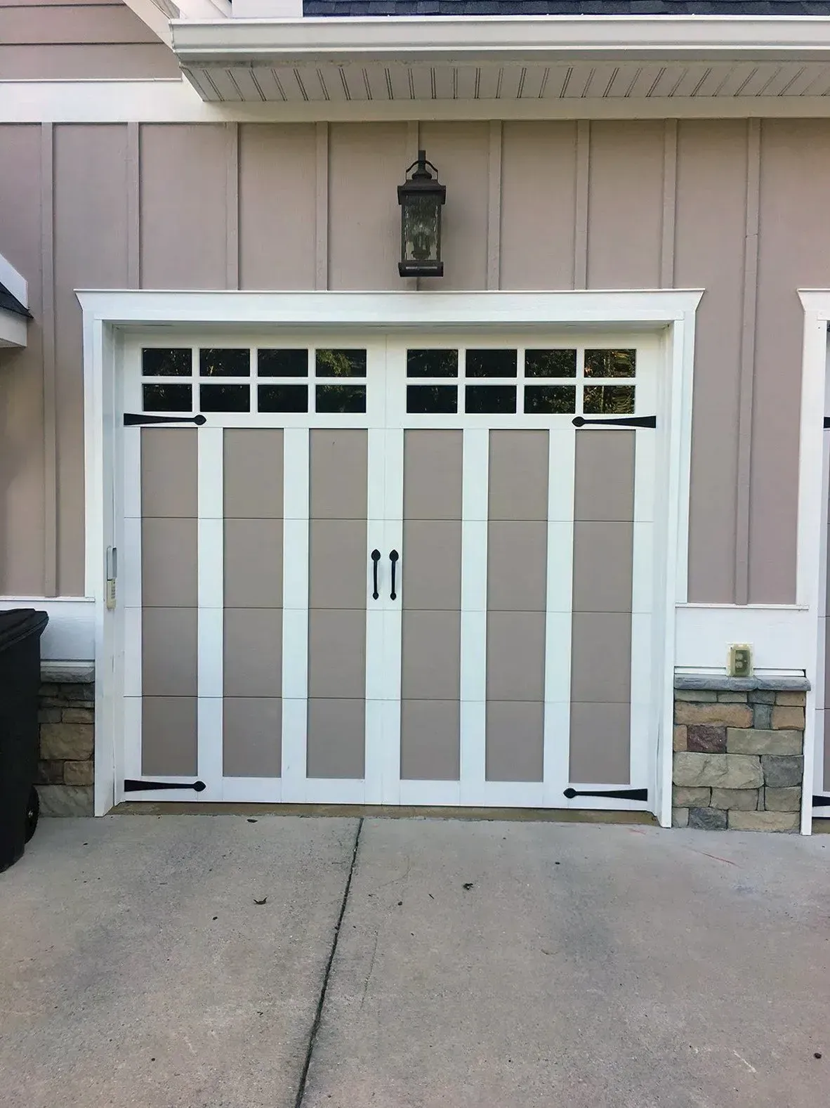 Tan garage door with white trim, black hardware, and upper windows.