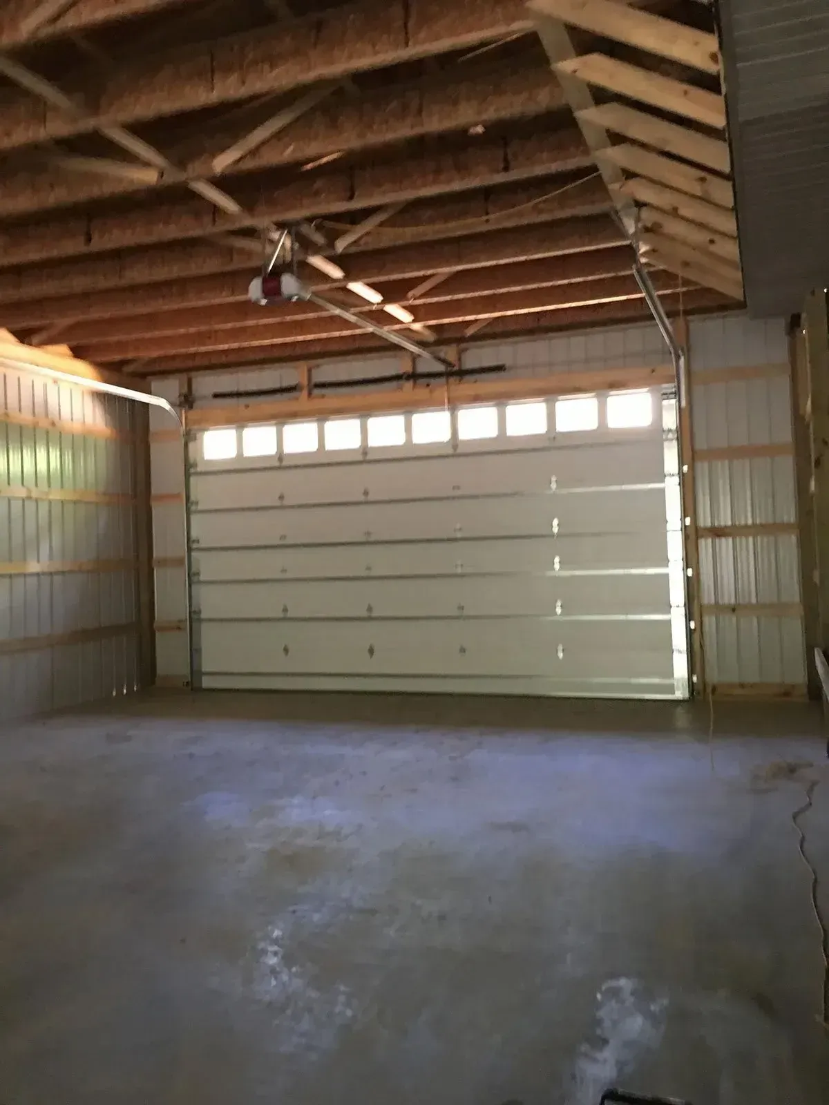 Interior of a garage with concrete floor and a partially open white garage door. Metal walls.