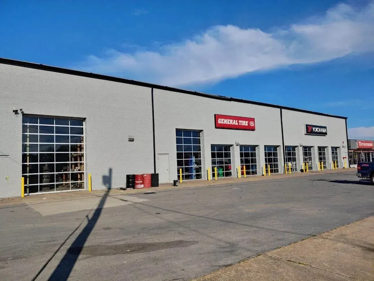 Exterior of a gray commercial building with several storefronts, including a red and white sign. Blue sky above.