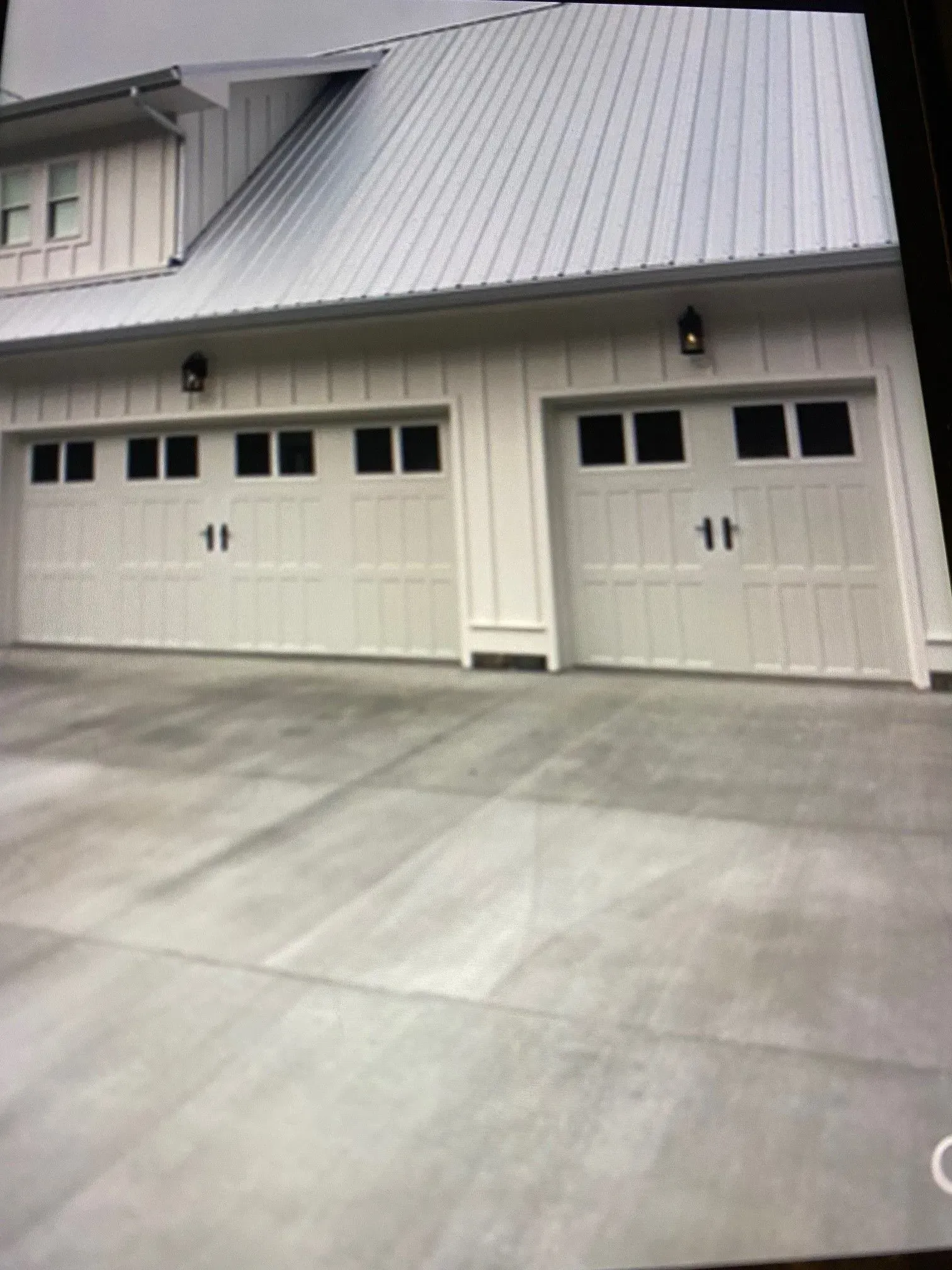 White garage doors on a modern house with a metal roof and concrete driveway.