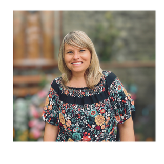 Woman with blonde hair wearing a floral top smiles outdoors.