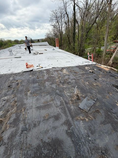 Flat rooftop under repair with white membrane, a worker, and trees in the background