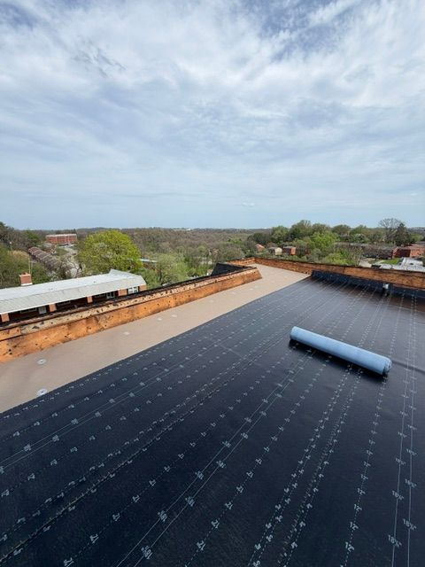 Rooftop under construction with dark waterproof membrane, rolled material, and a cloudy sky above.