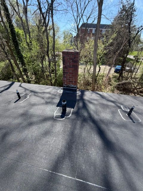 Flat rooftop with a brick chimney, roof anchors, and leafless trees casting shadows nearby.