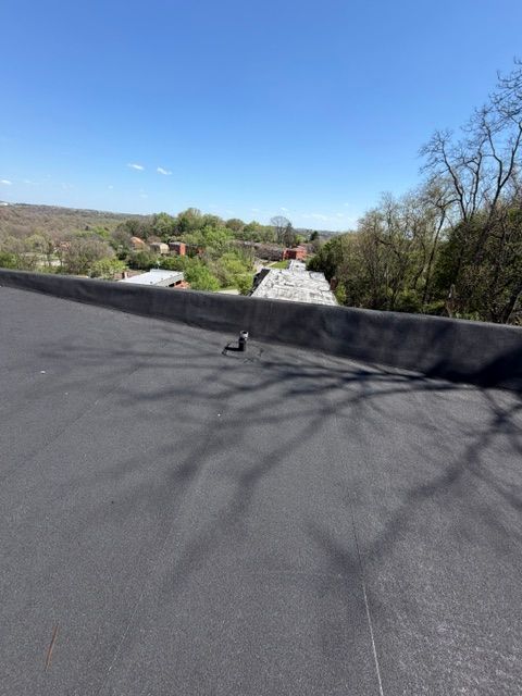 Flat black rooftop overlooking a rural valley with trees, houses, and a bright blue sky