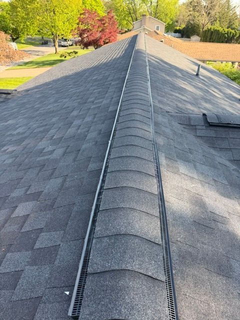 Roof ridge with dark gray shingles and ridge vent on a sunny house roof