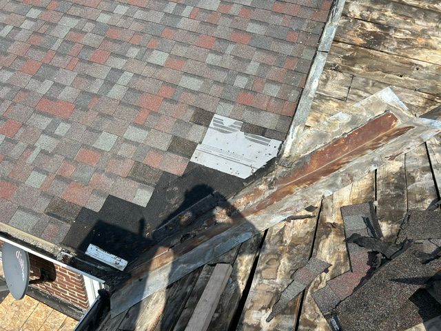 Damaged shingled roof beside a brick-paved area, with exposed wood and scattered debris