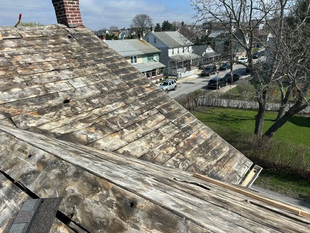 Weathered rooftop overlooking houses, trees, and a street on a clear day