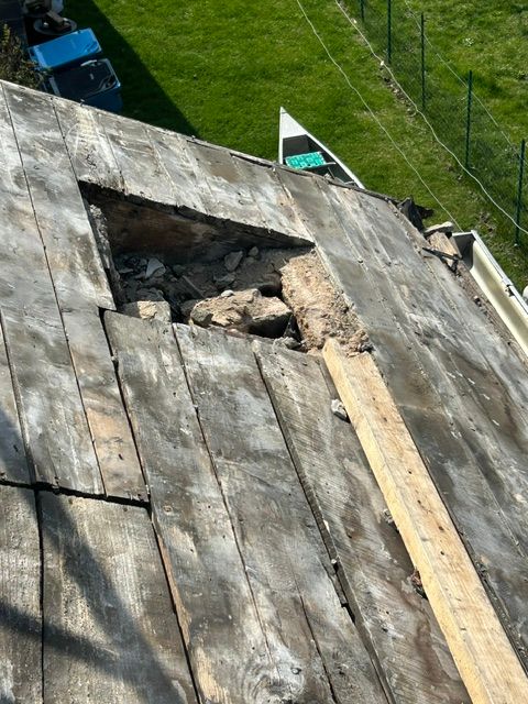 Damaged roof with a large hole, exposed wood, and a ladder against the shingles.