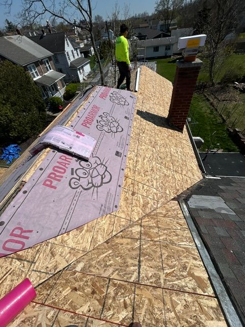 Roof under construction with worker, pink underlayment, and plywood sheathing on a sunny day