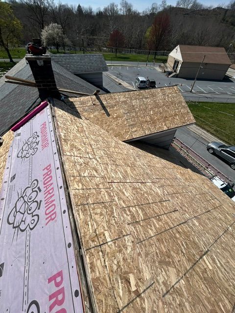 Roof under construction with plywood sheathing and pink underlayment beside neighboring houses