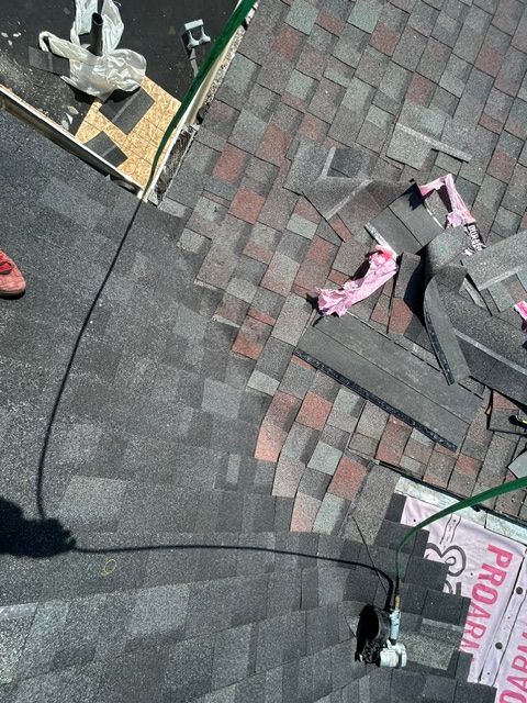 Rooftop with gray shingles, loose black panels, and pink insulation under repair near a vent and safety rope