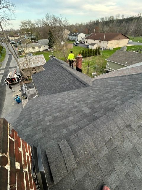 Workers installing dark gray shingles on a house roof in a suburban neighborhood