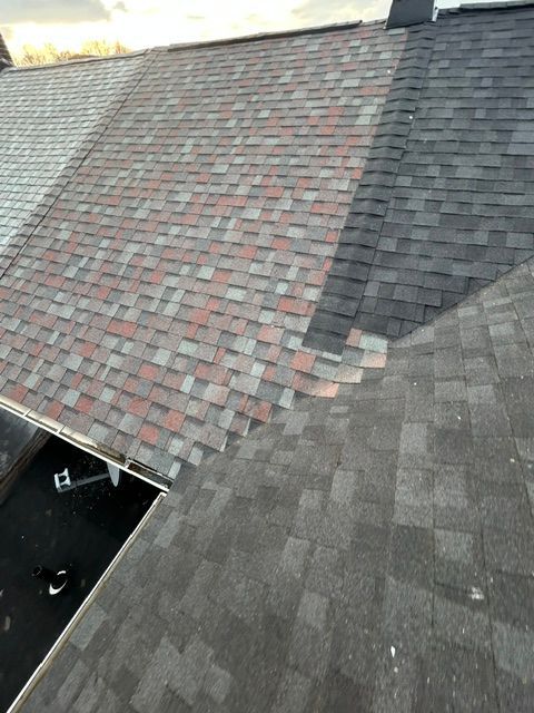 Roof with two shingle sections: red-gray pattern meeting dark gray shingles at a steep seam.