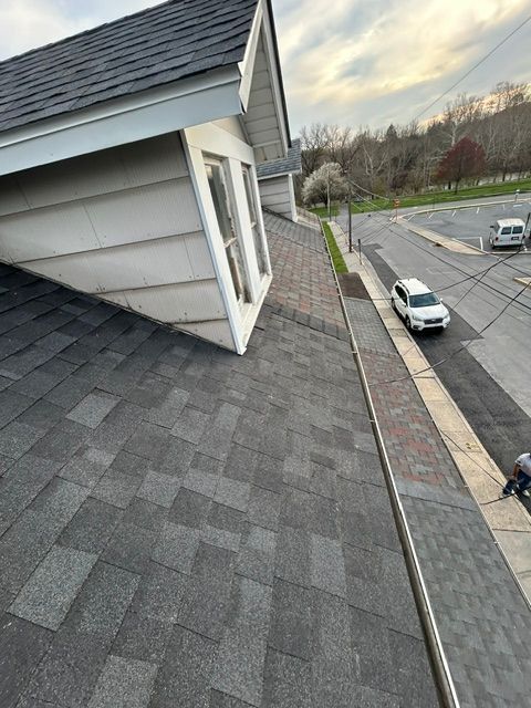 Rooftop view of gray shingles beside a suburban street with parked cars and a cloudy sky.