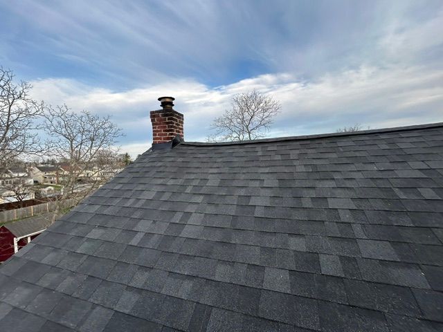 Dark shingled roof with a brick chimney under a cloudy sky