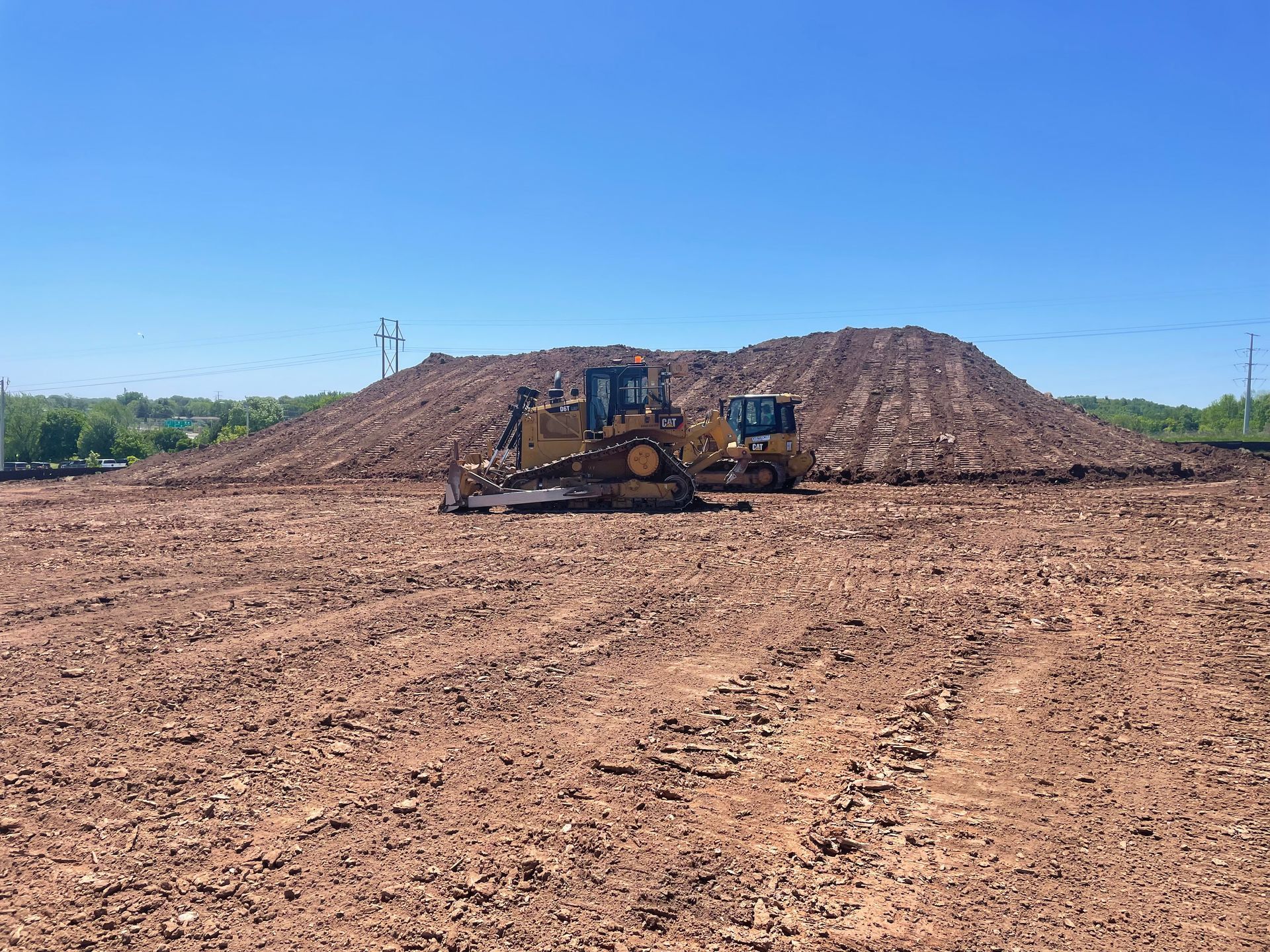 Two bulldozers are working in a dirt field next to a large pile of dirt.