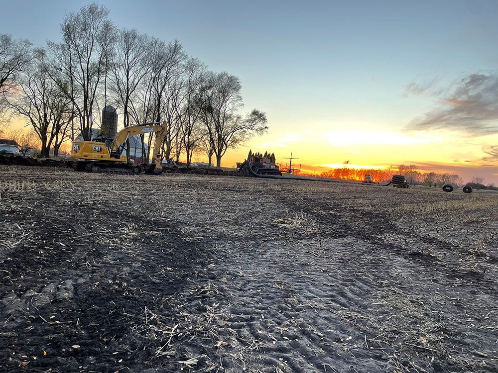 A large yellow excavator is parked in a dirt field at sunset.