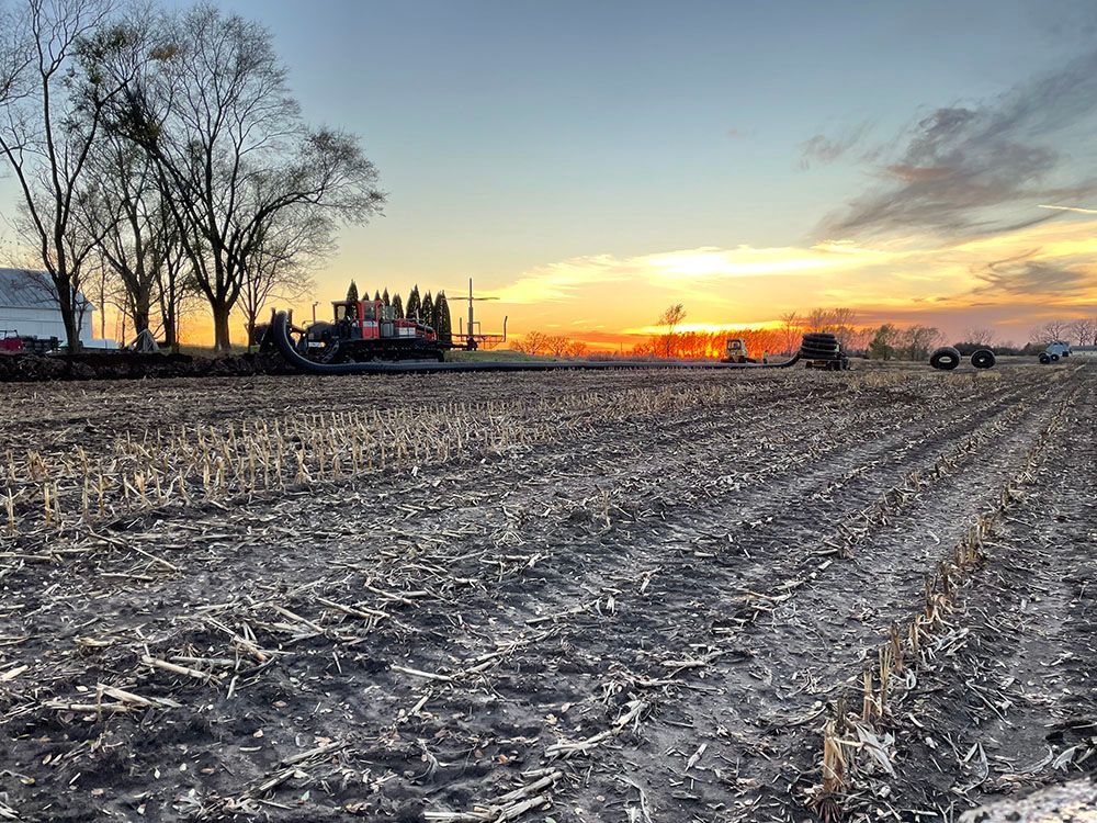 A field with a sunset in the background and a tractor in the foreground.