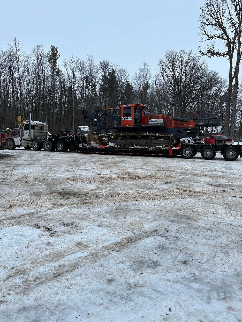 A large excavator is being transported on a trailer in the snow.