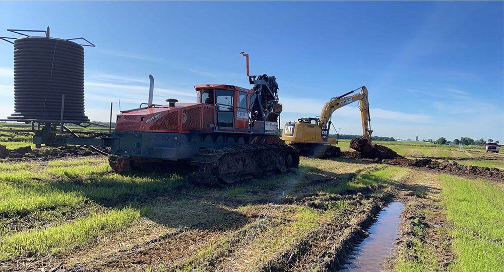 A bulldozer and an excavator are driving through a muddy field.
