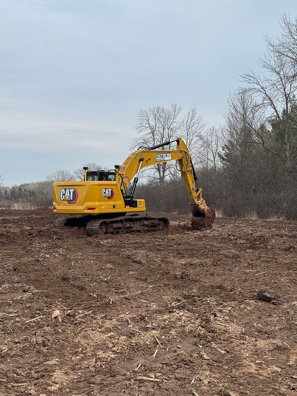 A yellow excavator is driving through a dirt field.
