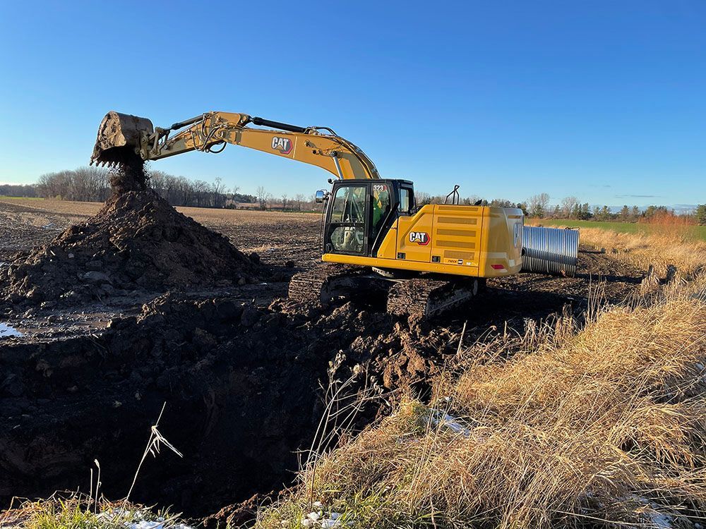 A yellow excavator is digging a hole in a field.