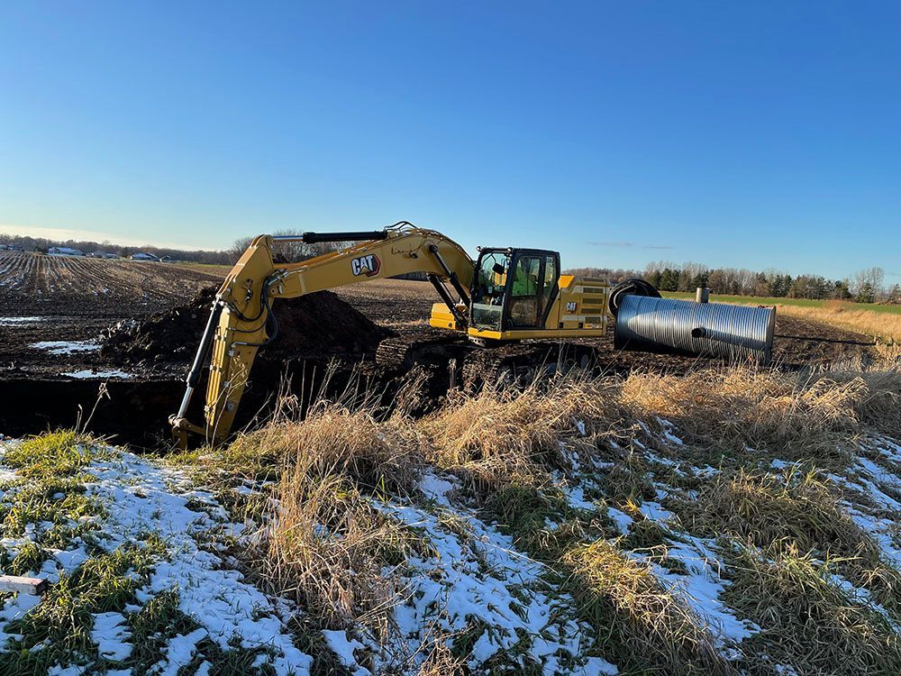 A yellow excavator is digging a hole in a field.