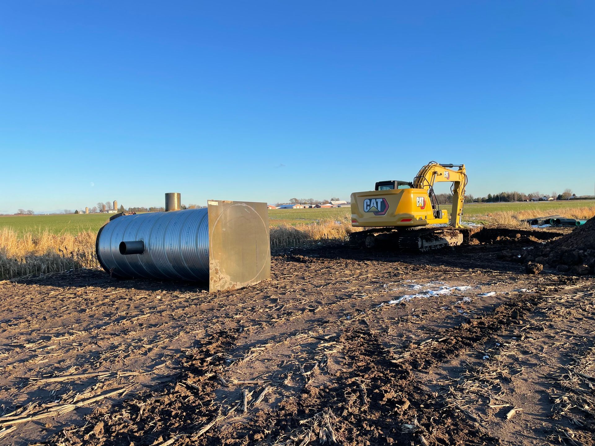 A yellow excavator is sitting in a dirt field next to a large metal pipe.