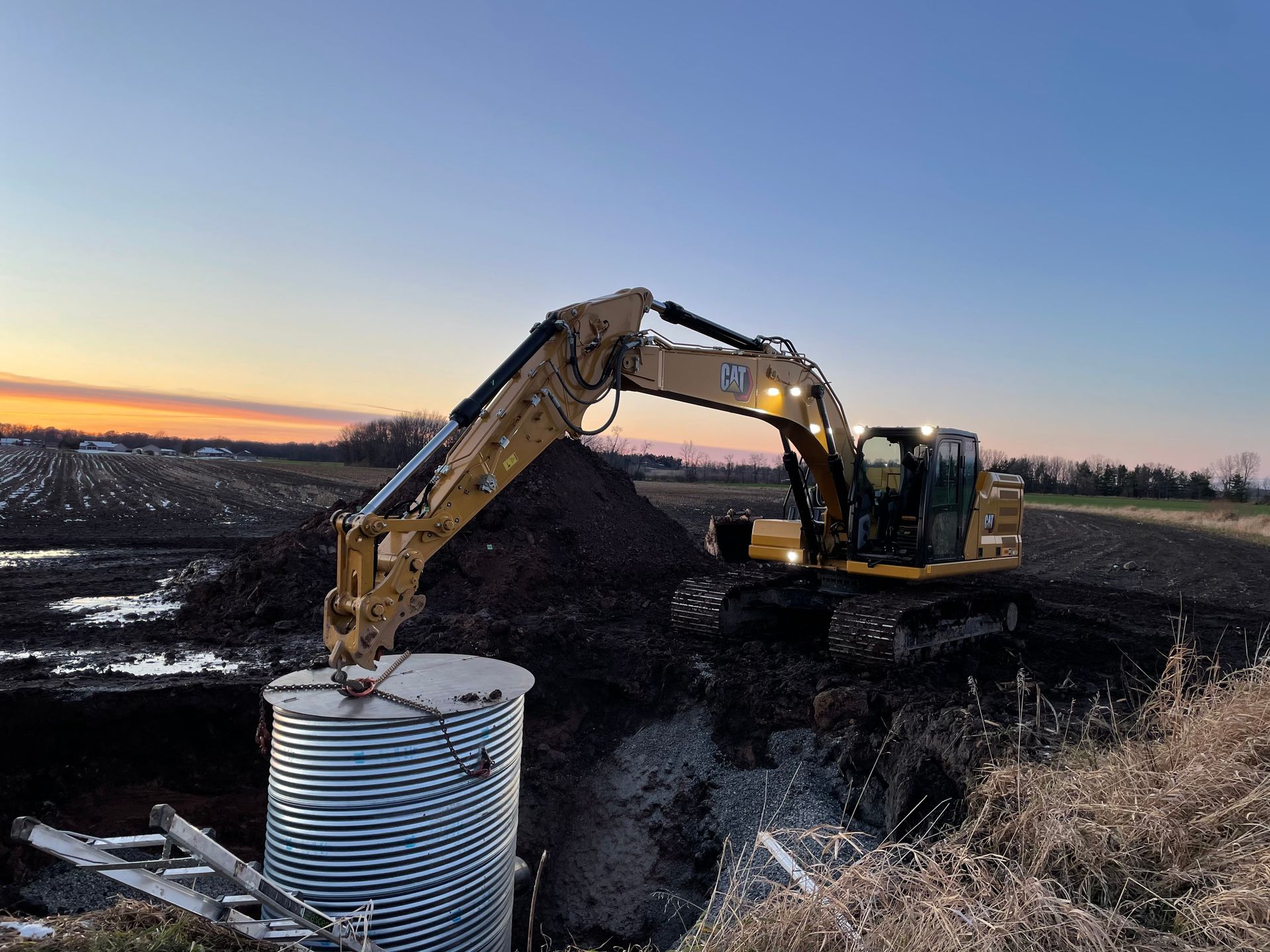 A large excavator is digging a hole in a field at sunset.