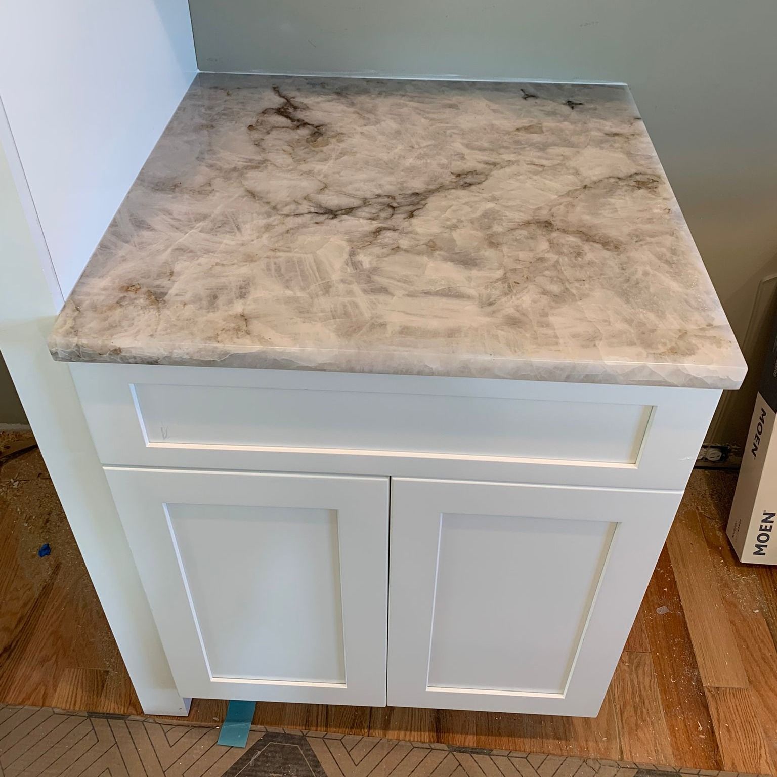 A white cabinet with a marble counter top is sitting on a wooden floor.