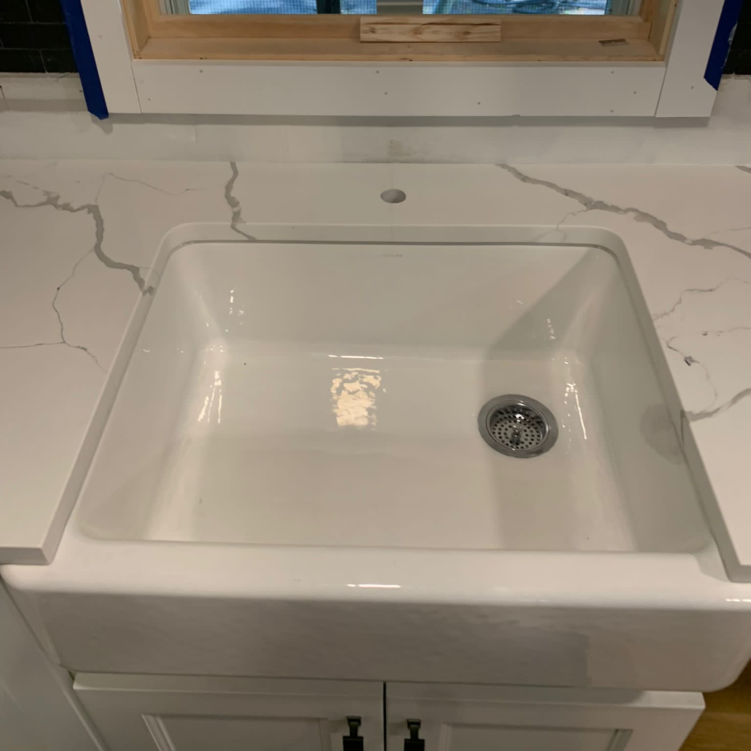 A white sink is sitting on top of a white counter next to a window.
