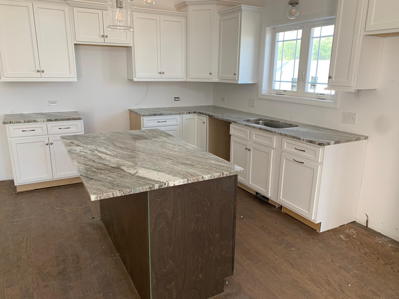 A kitchen with white cabinets , granite counter tops , and a large island.