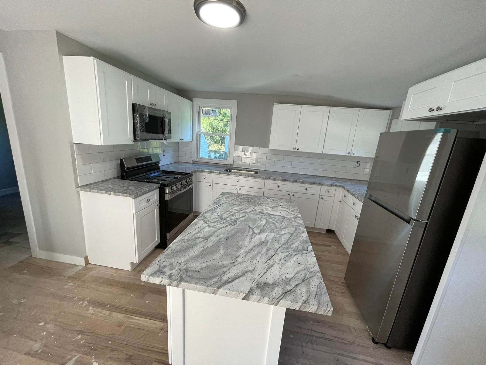 A kitchen with white cabinets , granite counter tops , stainless steel appliances and a refrigerator.