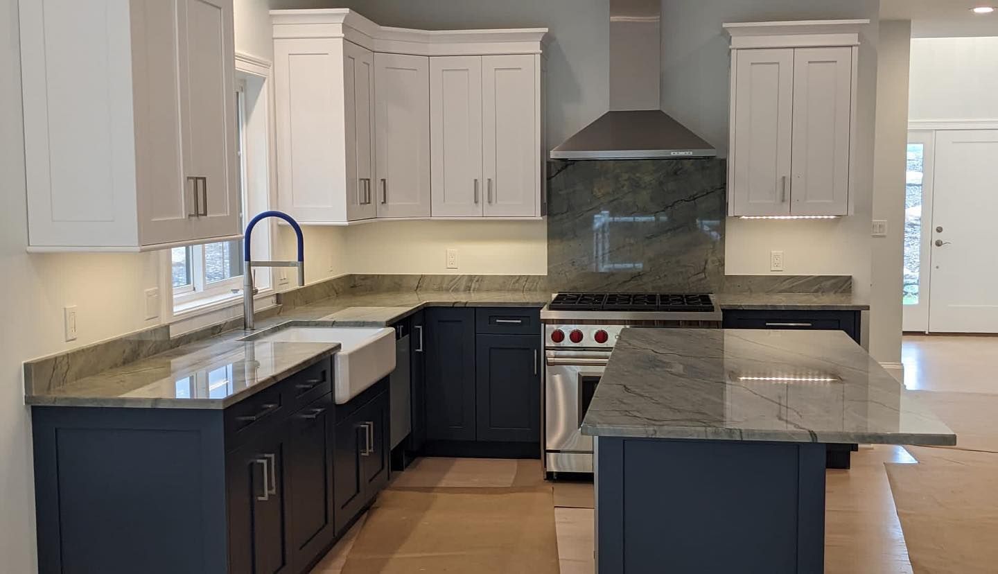 A kitchen with blue cabinets , white cabinets , granite counter tops , a stove and a sink.