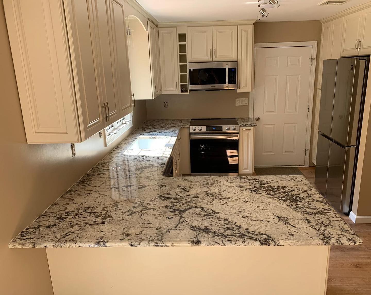 A kitchen with white cabinets , granite counter tops , a stove , refrigerator and microwave.
