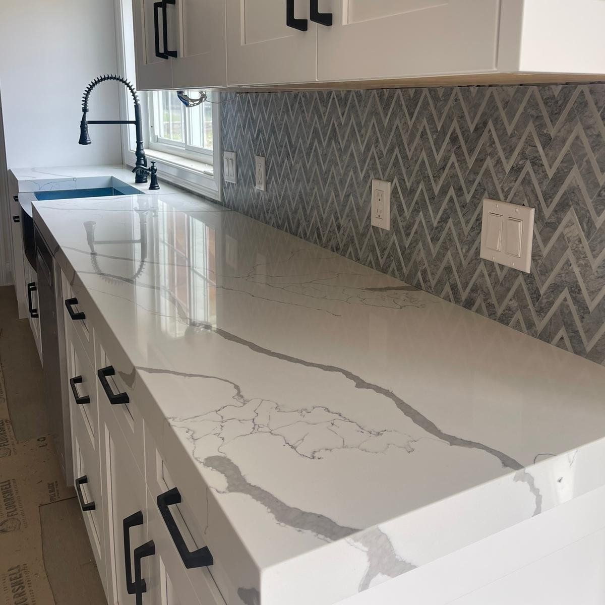 A kitchen with white cabinets , a sink , and a quartz counter top.