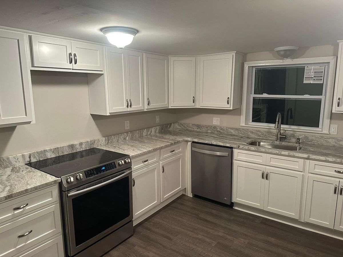 A kitchen with white cabinets , stainless steel appliances , granite counter tops and a window.