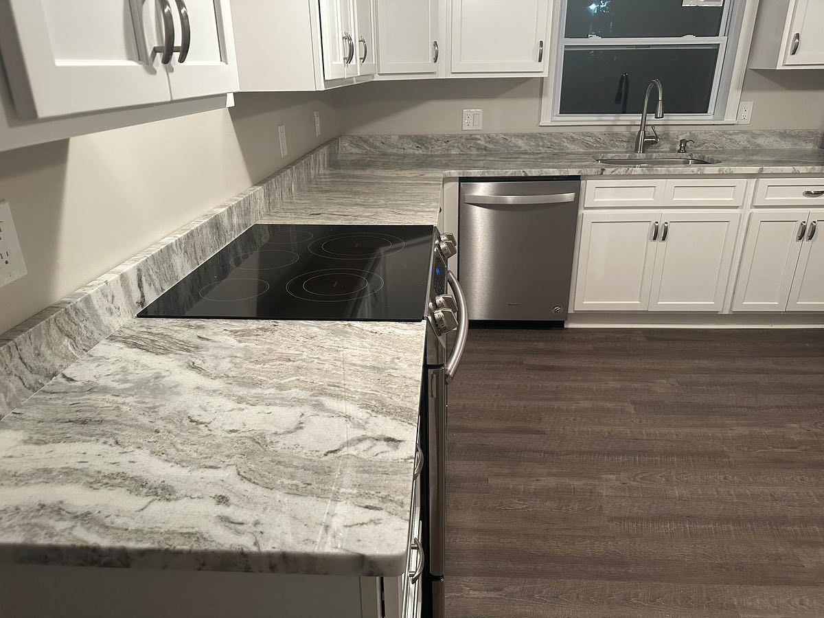 A kitchen with granite counter tops , stainless steel appliances , and white cabinets.