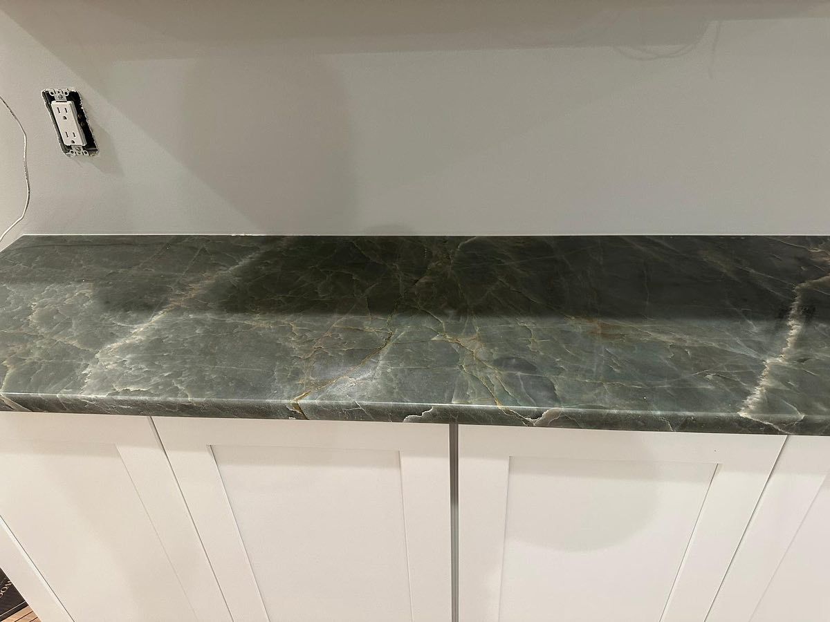 A kitchen counter with a green marble counter top and white cabinets.